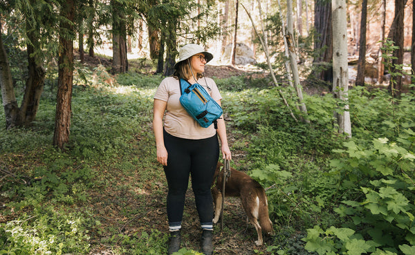 Person standing in the forest on a hiking trail, walking their dog on leash, wearing the LGD front-carry style.